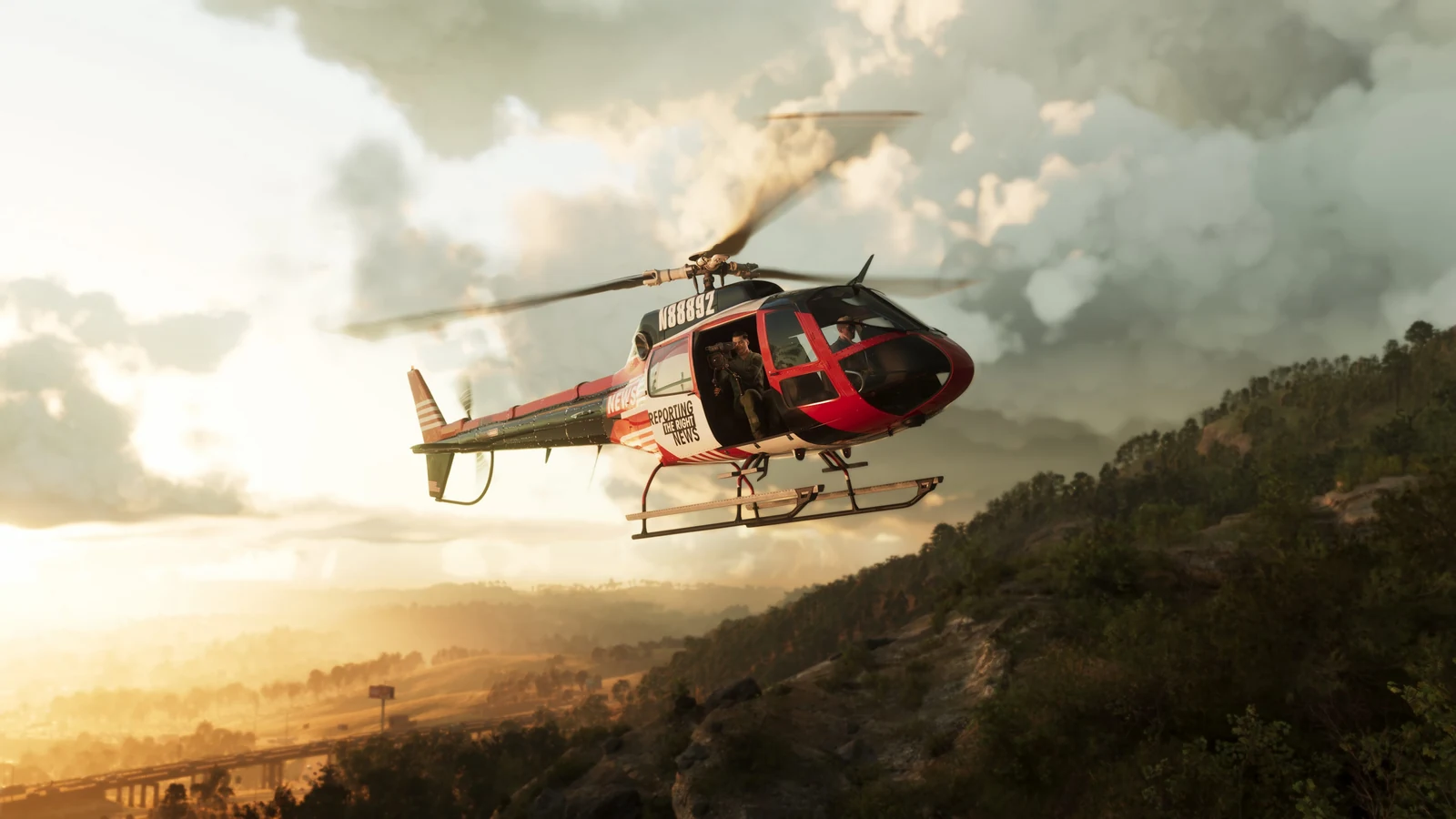 Red helicopter above wooded hills and a hazy sunlit valley.
