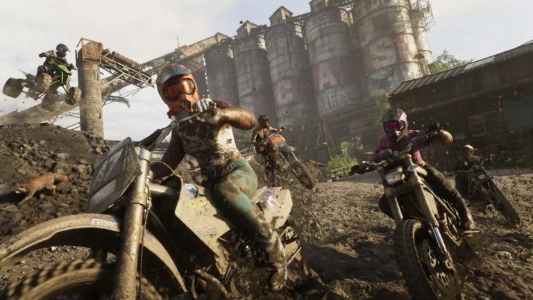 Helmeted riders race muddy dirt bikes and an ATV past a weathered industrial complex.