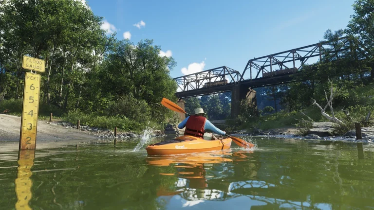 A kayaker in an orange boat paddles beneath a steel bridge on a wooded river.